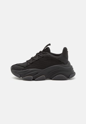 Baskets noires avec dessus en mesh et daim, semelle épaisse texturée et lacets plats. Le talon possède un col rembourré et un petit détail de logo.