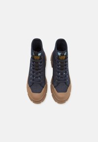 Zapatillas altas de tela azul oscuro con suelas de goma marrón, que presentan cordones negros y un panel de acento azul en la lengüeta.