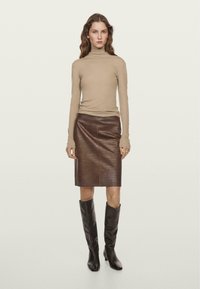 Pull à col roulé beige, ajusté ; jupe crayon en cuir marron avec un motif texturé ; bottes marron à hauteur de genou avec un bout pointu.