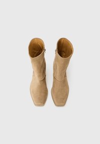 Bottines en suede beige à bout carré, avec un design rabattu et une fermeture éclair sur le côté. Texture lisse avec une apparence minimaliste.