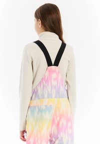 Farebné tie-dye overall v pastelových odtieňoch s rebrovaným rolákom pod nimi. Nastaviteľné čierne popruhy a bezšvový dizajn chrbta.