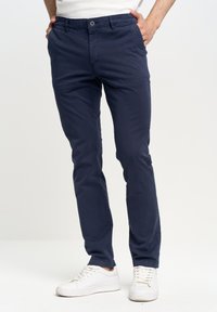 Morske modre hlače iz mešanice bombaža s slim fit krojem. Imajo gumbasto zapiranje, stranske žepe in so stilizirane z belimi superge.