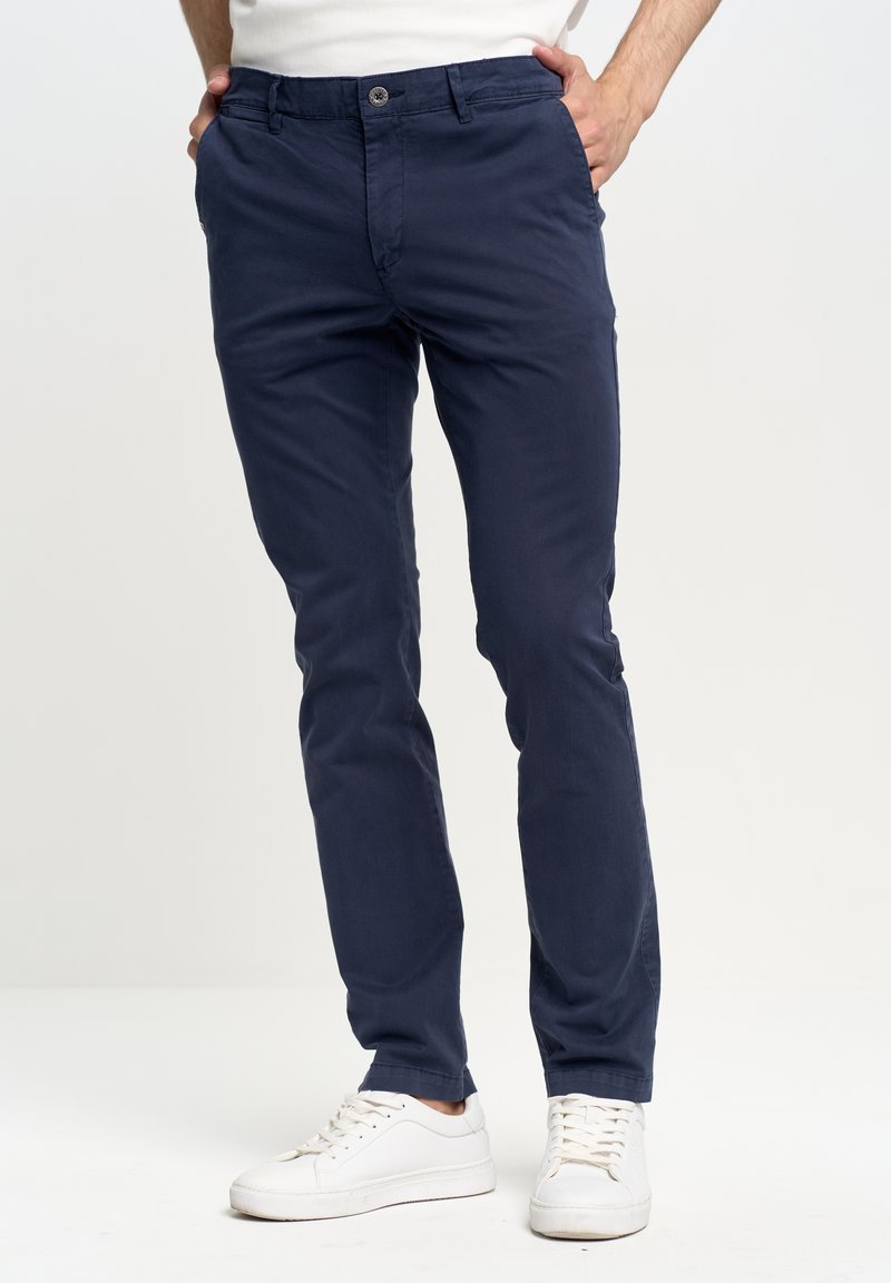 Morske modre hlače iz mešanice bombaža s slim fit krojem. Imajo gumbasto zapiranje, stranske žepe in so stilizirane z belimi superge.