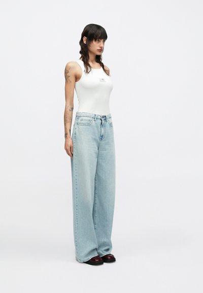 Λευκό φανελάκι με λογότυπο, ανοιχτό μπλε ψηλόμεσο τζιν με φαρδιά μπατζάκια και σκούρα κόκκινα πλατφόρμα παπούτσια. Λείο ύφασμα και άνετη εφαρμογή.