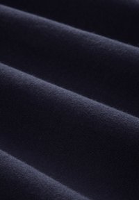 Měkká, tmavě modrá tkanina s viditelnou jemnou texturou, zachycena v detailním záběru záhybů, které zvýrazňují hladký, hustý materiál a jemné odlesky světla.
