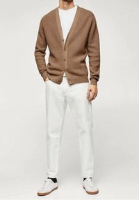 Hnědý pletený cardigan s výstřihem do V a pěti knoflíky, kombinovaný s bílými džíny a bílými teniskami. Textura je mírně vyvýšená.