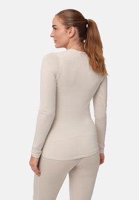 Langärmliges, enganliegendes Oberteil in hellem Beige, aus glattem Stoff gefertigt. Verfügt über einen runden Ausschnitt und ein nahtloses Design für Komfort und Flexibilität.