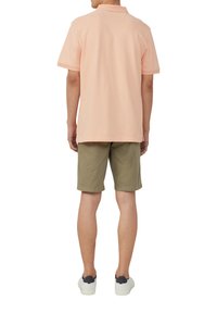 Lichtroze polo shirt met korte mouwen, gecombineerd met olijfgroene shorts en witte sneakers met donkere accenten. Zicht van achteren.