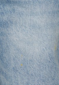 Tela de mezclilla de un azul claro con sutiles patrones de desgaste y pequeñas manchas de pintura amarilla en la superficie.