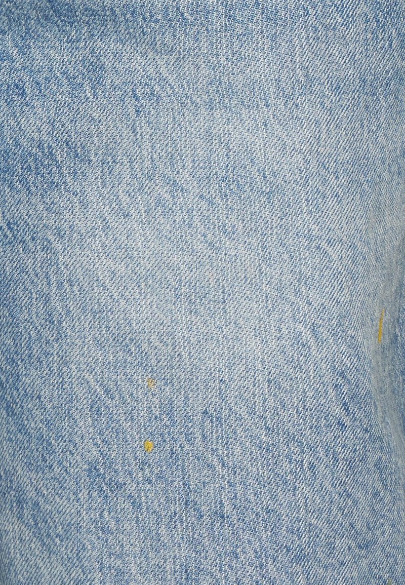 Tela de mezclilla de un azul claro con sutiles patrones de desgaste y pequeñas manchas de pintura amarilla en la superficie.