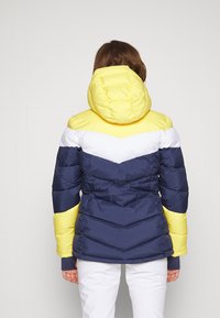 Piumino a blocchi di colore con giallo, bianco e blu navy. Colletto alla coreana e cappuccio, con motivo trapuntato a chevron. Tessuto dalla texture.