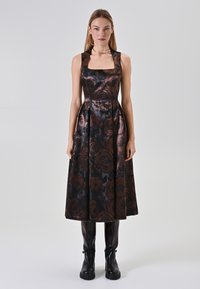 Schwarzes Blumenkleid mit quadratischem Ausschnitt und ausgestelltem Rock, verziert mit bronzefarbenen Rosenmustern und transparenten Trägern. Kombiniert mit schwarzen Ankle Boots.