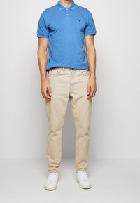 Světle modrá bavlněná polo tričko s krátkými rukávy, zkombinované s béžovými denimovými džíny a bílými teniskami. Diskrétní logo na tričku.