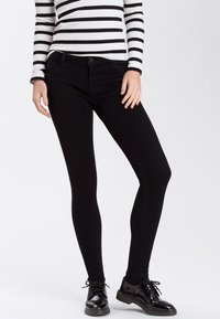 Czarne wąskie dżinsy z elastycznej bawełnianej mieszanki. Posiadają klasyczny fason z pięcioma kieszeniami i dopasowany krój. Noszone z paskowanym topem i czarnymi butami.