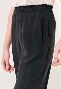 Zwarte, lichte broeken met een ontspannen pasvorm. Voorzien van een elastische tailleband en zachte, gladde stof met subtiele plooien.