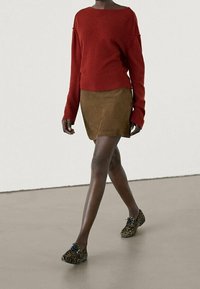 Pull en maille rouge à épaules tombantes, mini-jupe en daim marron et chaussures imprimé léopard avec lacets noirs. Tenue simple et décontractée.