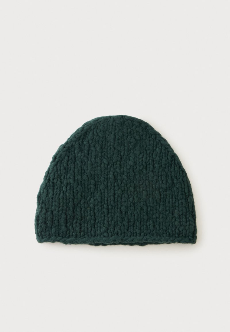 Bonnet en grosse maille vert foncé avec un dessus arrondi, présenté à plat sur un fond clair.