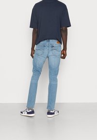 Světle modré džíny s rovný fit, s hnědou koženou nášivkou a zadními kapsami, v kombinaci s námořnickým tričkem a teniskami.