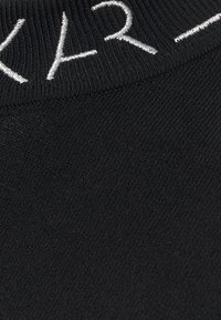 Tissu tricoté noir avec détails de couture visibles et lettres blanches partiellement brodées près du bord.