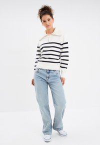 Pull blanc avec des rayures marine, col zippé et ourlet côtelé. Associé à un jean bleu clair à coupe ample et des baskets blanches.
