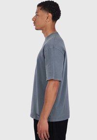 Grå kortærmet t-shirt lavet af blød bomuld. Har en rund hals, løs pasform og en diskret logo-detalje på ærmet. Rent design.