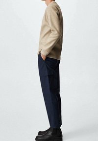 Beżowa bluzka z długim rękawem o luźnym kroju, zestawiona z granatowymi spodniami typu cargo z bocznymi kieszeniami, uzupełniona czarnymi botkami za kostkę. Prosty, nowoczesny design.