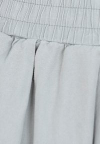 Jasnoszara tkanina o teksturowanej powierzchni. Posiada marszczoną gumkę w talii i marszczenia, tworzące miękkie fałdy.