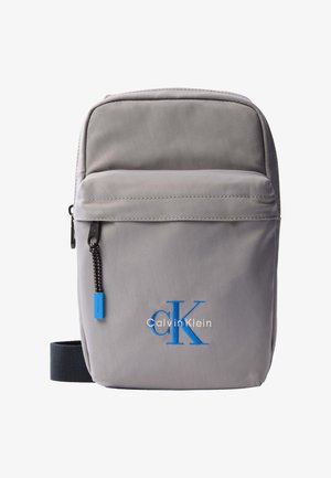 Kis szürke Calvin Klein keresztpántos táska elülső cipzáras zsebbel, fekete pánttal és kék „cK” logóval hímezve.