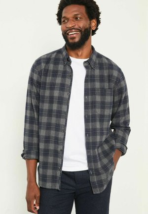 Gray and navy plaid flannel shirt with a button-up design, chest pocket, and rolled sleeves over a white t-shirt.