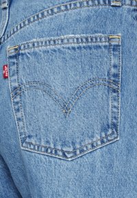 Poche arrière d'un jean en denim bleu avec une couture double en forme d'arche distinctive et une petite étiquette en tissu rouge sur le côté gauche.