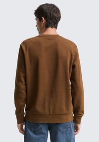 Bruin pullover sweatshirt met een ronde hals, gemaakt van een zachte stof, met lange mouwen en een geribbelde zoom. Draagt bij blauwe jeans.