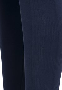 Tmavě modré legíny vyrobené z elastické látky, s hladkým povrchem a žebrovanou texturou, mírně lesklé a minimalistického designu.