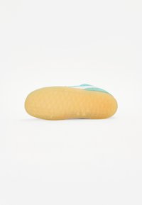 Sola do sapato em borracha castanha clara, com um padrão texturizado e formas geométricas. Parte superior visível em cores aqua e branca.