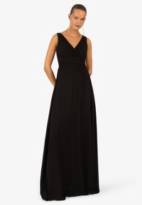 Czarna wieczorowa suknia z płynnej tkaniny. Posiada dekolt w serek, bez rękawów oraz marszczony bodice, tworząc elegancką sylwetkę.
