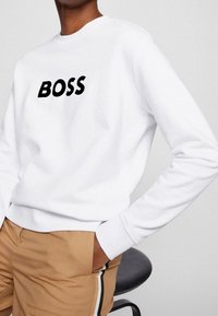 Vit sweatshirt i bomullsmix med en svart "BOSS"-logotyp på framsidan. Den har rund halsringning och långa ärmar.