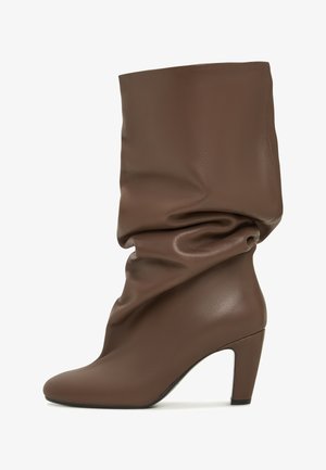 Brązowy, luźny botek do kostki wykonany z gładkiej skóry. Charakteryzuje się okrągłym noskiem oraz obcasem. W designie uwzględniono miękkie fałdy wokół górnej części cholewki.