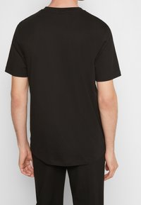 Svart bomullströja med rundad halsringning, korta ärmar och rundad nederkant. Tyget verkar slätt med en klassisk passform.