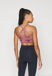 Sutien sport tie-dye bordo, cu design racerback și mai multe bretele. Asortat cu colanți negri cu talie înaltă. Textură fină.