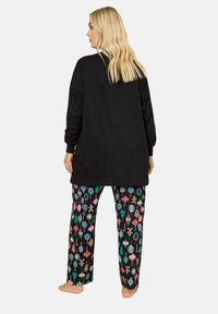 Musta pitkähiha paita yhdistettynä kuviollisiin pyjamasortseihin, joissa on värikkäitä koristeita mustalla taustalla. Pehmeä kangas, rento istuvuus.