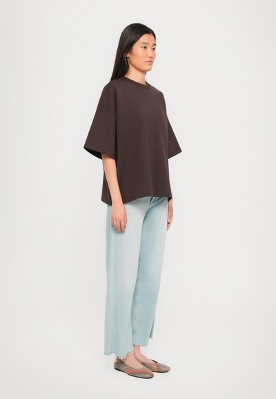 T-shirt marrone oversize con maniche corte, abbinato a jeans a gamba larga blu chiaro. Le calzature presentano un motivo a strisce multicolore.