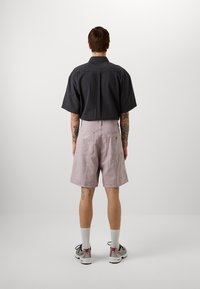 Kortermet svart teksturert skjorte, kombinert med lyserosa shorts med lommer, hvite sokker og grå-røde sneakers.