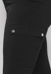 Pantaloni cargo neri con tasca laterale e accessori in argento. Realizzati in un materiale liscio e resistente, presentano un design aderente.