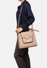 Borsa a tracolla in pelle beige con chiusura a pattina, dettagli in contrasto scuri e tracolla regolabile. Caratterizzata da un semplice accento in metallo argento.