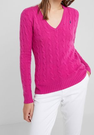 Roze kabelgebreide trui met een V-hals en geribbelde manchetten, met een aansluitend ontwerp en een textuurpatroon. Gecombineerd met witte broek.