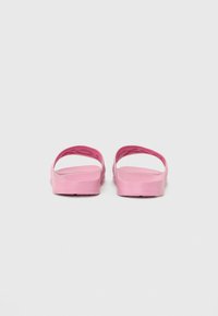 Roze gumijasti sandal s minimalističnim dizajnom, širokimi naramnicami in ravnim podplatom, ki prikazuje gladko teksturo in preprosto silhueto.