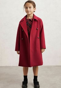 Rød uldfrakke med dobbeltradet design, store revers og dekorative knapper. Båret over en ternet kjole og parret med sorte strømper og sko.