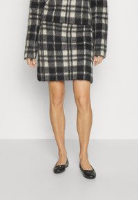 Svart- och vitrutigt kjol i mjukt, fluffigt material, med rak skärning och fåll ovanför knät, tillsammans med svarta platta skor.