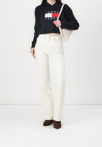 Czarny prążkowany krótki sweter z logo, zestawiony z białymi jeansami o wysokim stanie. Brązowe botki na obcasie oraz mała beżowa torebka wchodzą w skład stylizacji.