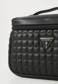 Borsa nera in ecopelle con design trapuntato, logo triangolare in metallo e chiusura con zip; presenta una superficie texturizzata e bordi arrotondati.