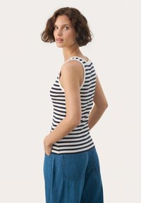 Striped tank top in navy and cream, ribbed texture, fitted design, with wide shoulder straps and rounded neckline. Worn with loose blue pants.